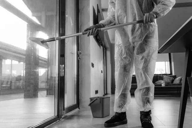 A person in a protective suit cleans glass doors indoors, emphasizing hygiene. Lokalvård i verksamheter: krav, avtal och uppföljning
