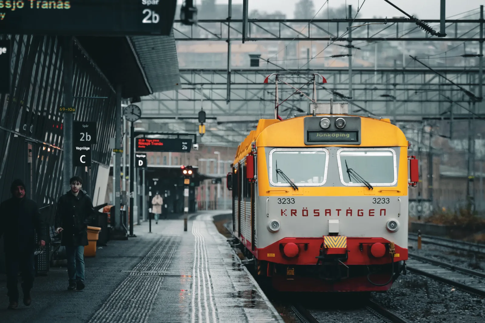A vibrant train at Jönköping station on a cloudy day in Sweden, capturing Nordic architecture.